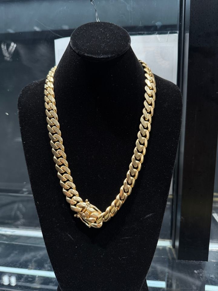 Cadena Miami cubana gruesa en oro amarillo, colgada en un busto de terciopelo negro.