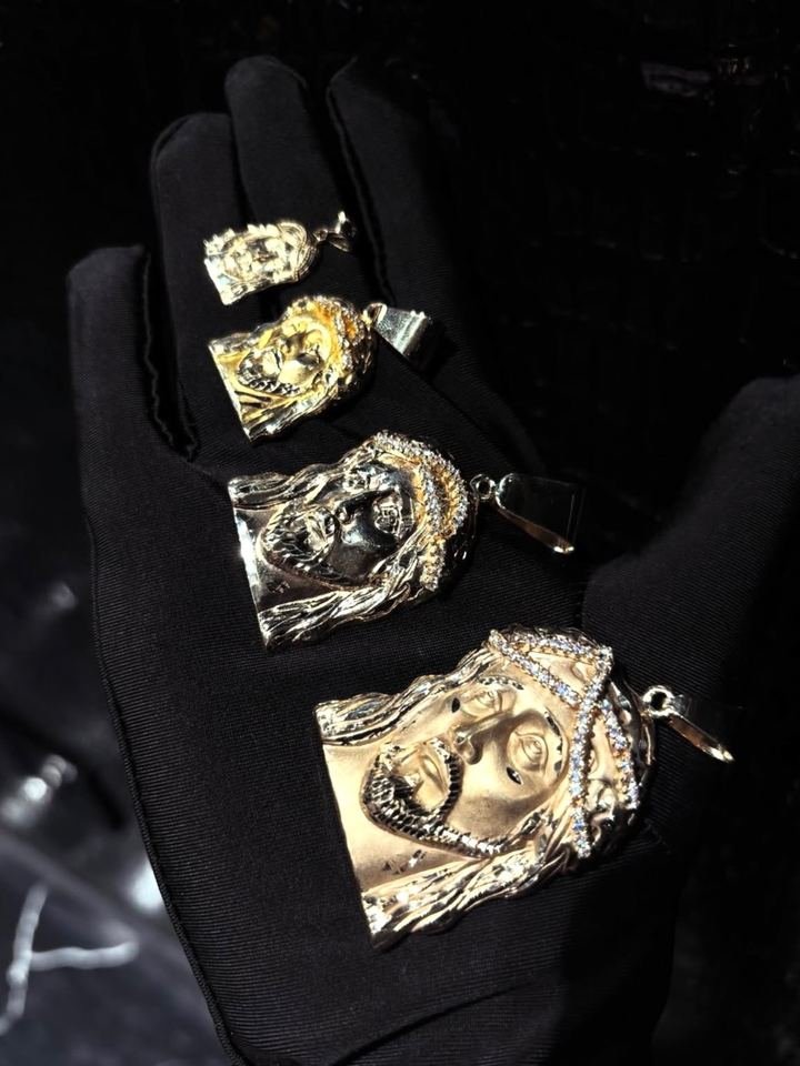 Cuatro dijes con el rostro de Cristo en oro, de menor a mayor, sostenidos en una mano con guante negro.