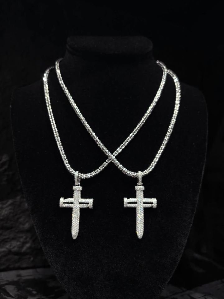Dos cadenas de tenis cruzadas, cada una con un dije de cruz cubierto de piedras blancas, sobre un busto de terciopelo negro.