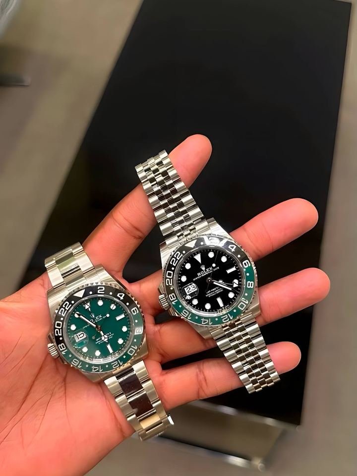 Dos relojes Rolex sostenidos en una palma desnuda, uno de esfera verde y otro de esfera negra, los dos con bisel verde y negro.
