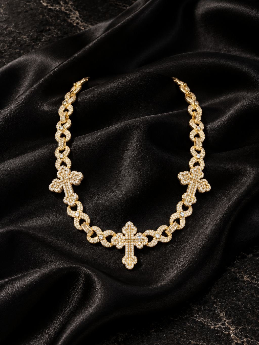 Yellow gold infinity-link chain with three clear-stone crosses, on black satin.