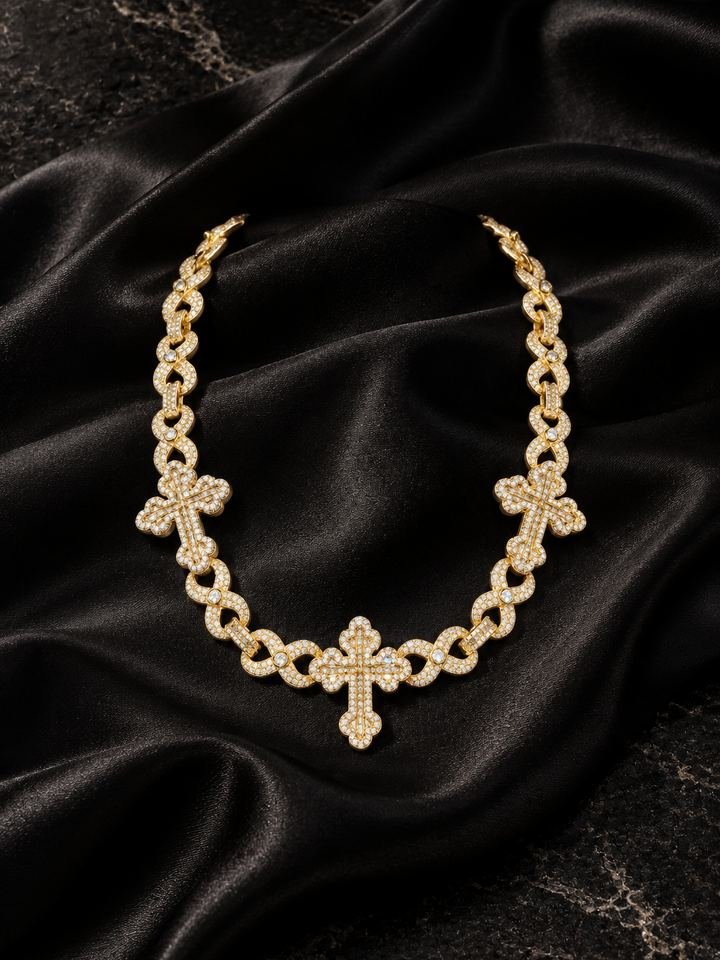 Cadena de eslabones en forma de infinito en oro amarillo con tres cruces de piedras claras, sobre satén negro.