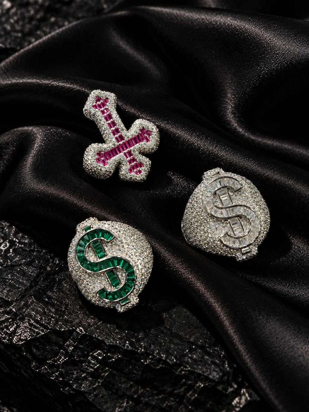 Three rings set with colored stones, one shaped as a cross and two as dollar signs, on black satin.