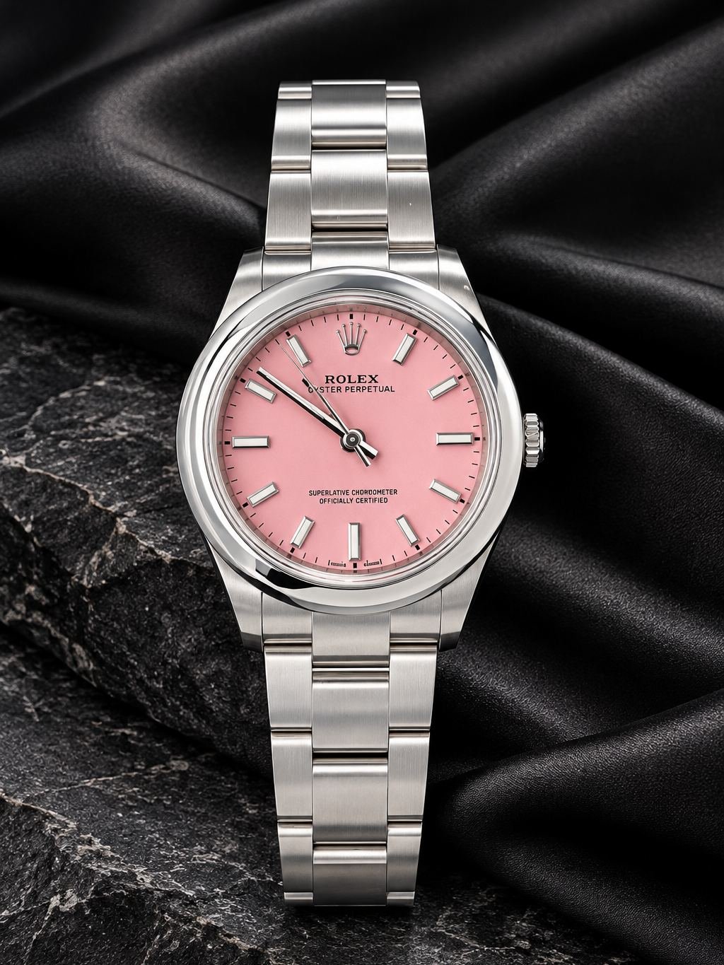 Reloj Rolex de acero con esfera rosa, sobre satén negro y piedra oscura.