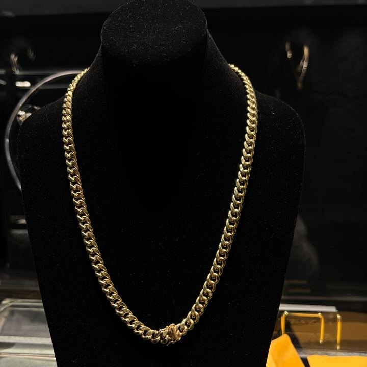 Cadena de eslabón cubano en oro amarillo, colgada en un busto de terciopelo negro dentro de la vitrina.