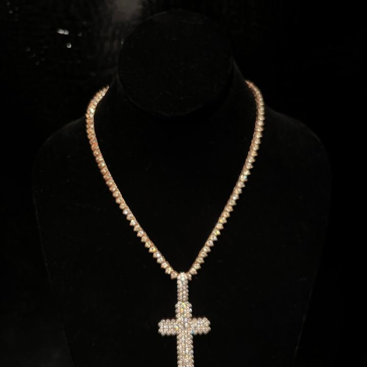 Cadena en oro rosa con un dije de cruz colgando, sobre un busto de terciopelo negro.