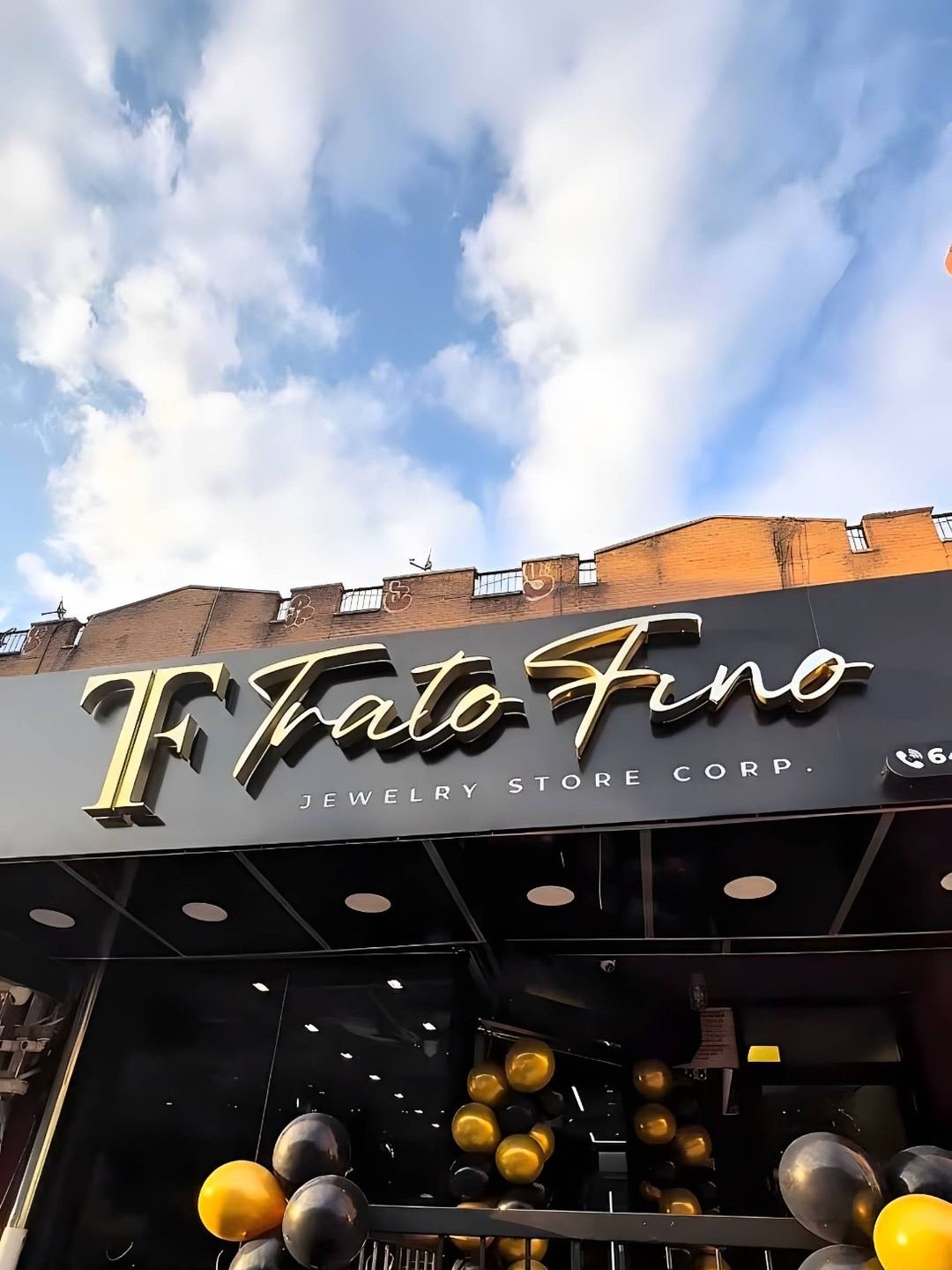 Fachada de la tienda en contrapicado, con el rótulo dorado Trato Fino sobre la entrada y columnas de globos negros y dorados en la puerta.